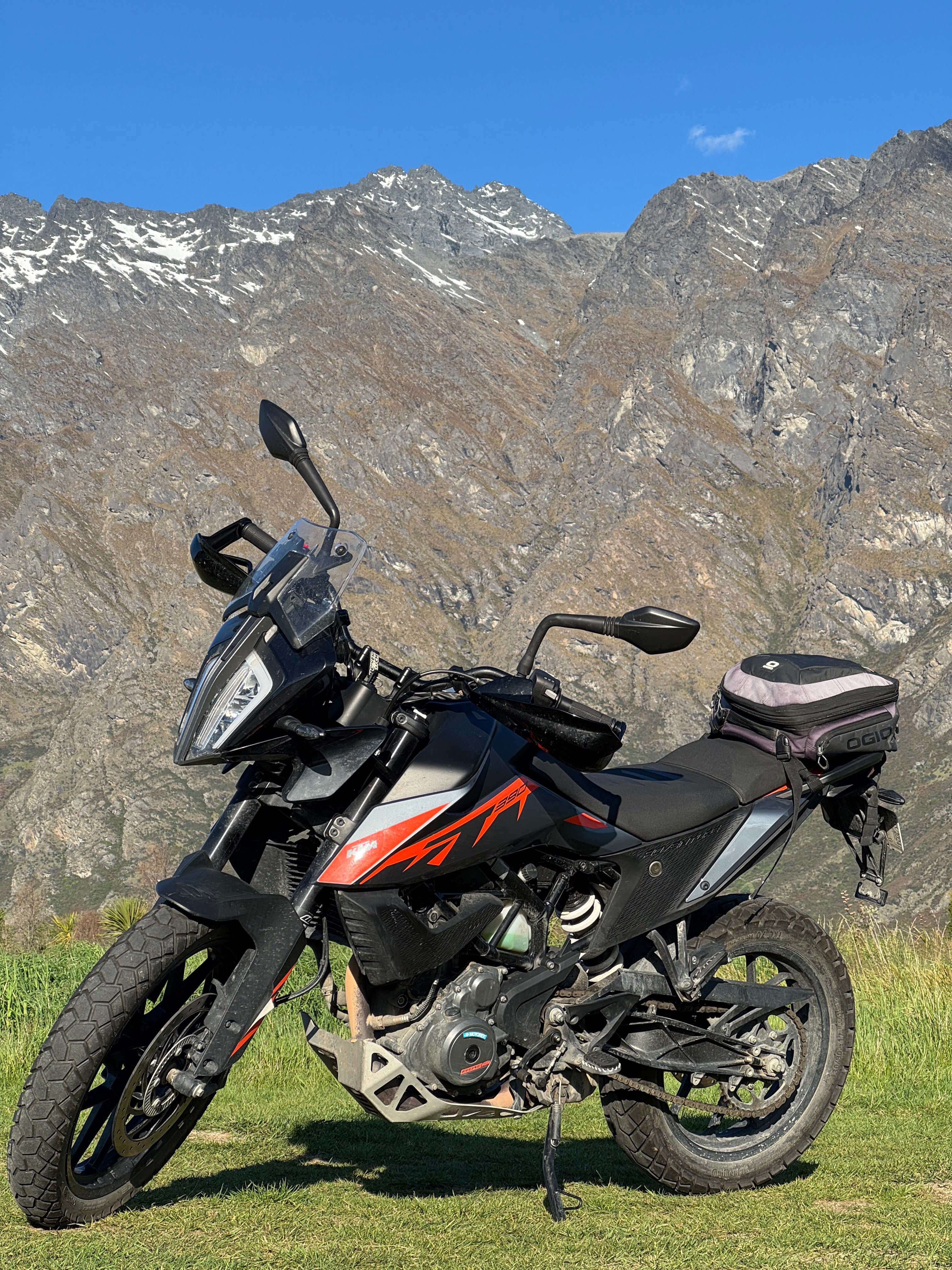 Rental Motorcycle with luggage on a grassy area with mountains in the background