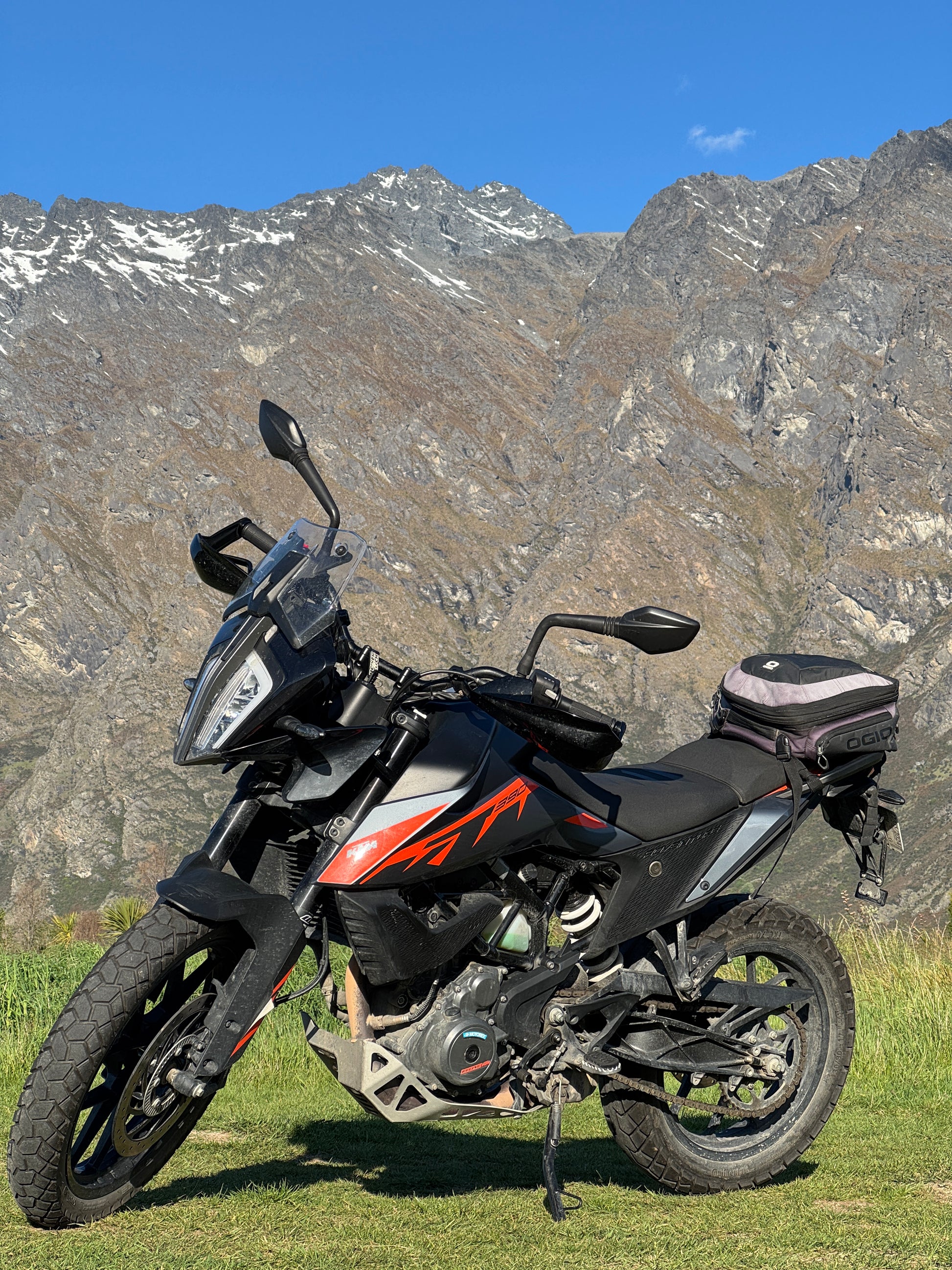 Rental Motorcycle with luggage on a grassy area with mountains in the background