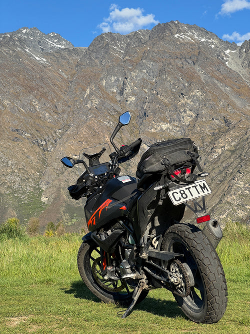 Rental Motorcycle with a black saddlebag on a grassy area with mountains in the background